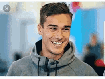 a man wearing a grey hoodie is smiling with an x on the bottom right