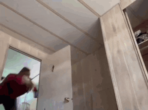 a woman in a red shirt is standing in a room with a door open