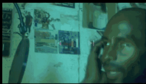 a man talking on a cell phone in front of a wall with posters on it