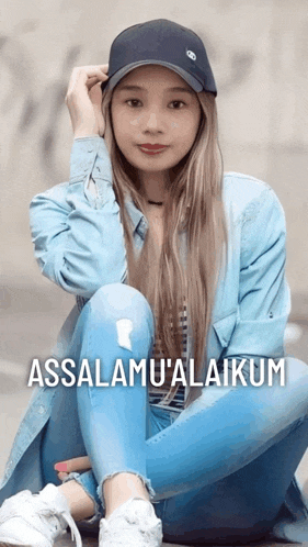 a woman wearing a blue jacket and a black hat sits on the ground with the words assalamu ' alaikum above her