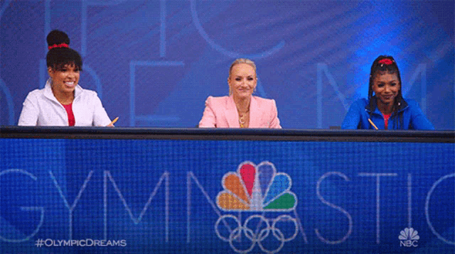 three women are sitting at a table with the word gymnastics written on it
