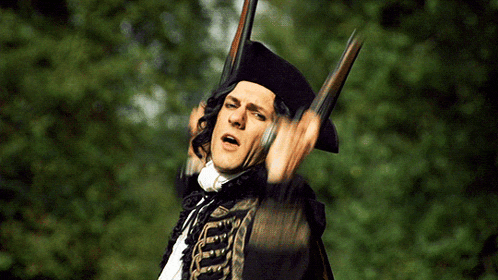 a man in a black hat is holding two guns in front of his face