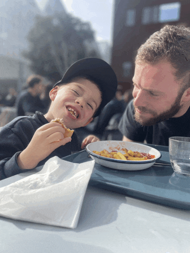 a man and a child are sitting at a table with a plate of food in front of them
