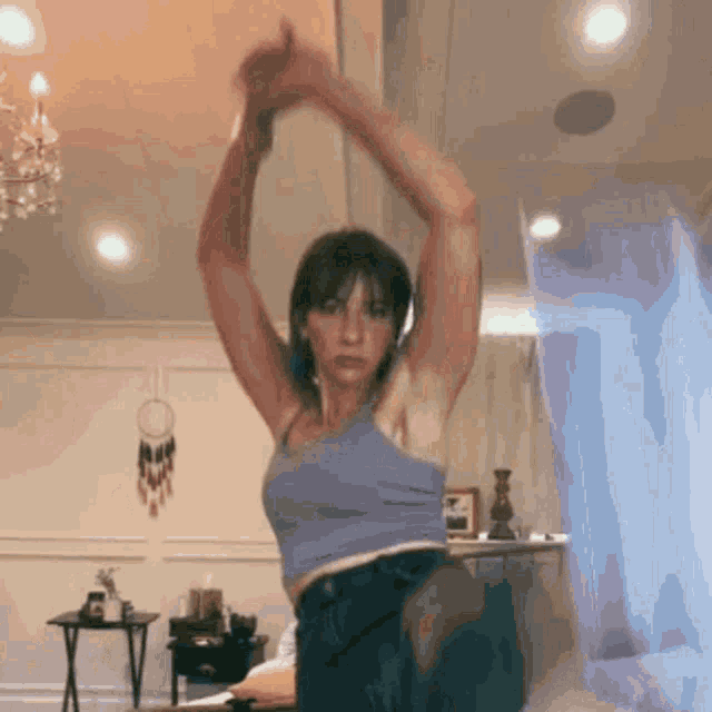 a woman in a blue tank top stretches her arms in a bedroom