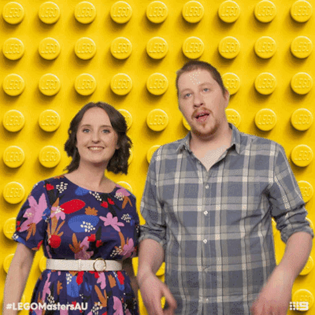 a man and a woman are posing in front of a wall of yellow lego bricks