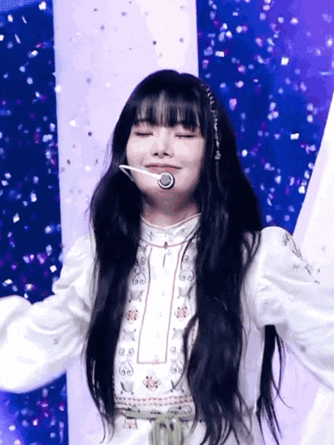 a woman with long black hair is wearing a white dress and a microphone