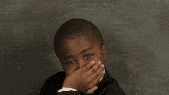 a young boy wearing a suit and tie is covering his nose with his hand