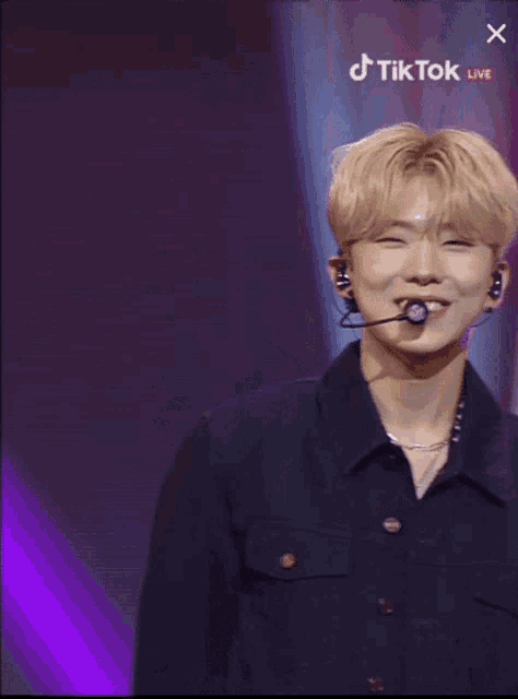 a man wearing a microphone and a black jacket is smiling and giving the peace sign