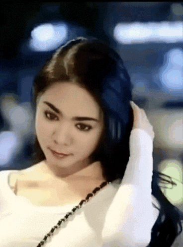 a woman in a white shirt is holding her hair in her hand