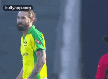 a man in a yellow and green jersey is clapping his hands while playing a game of cricket .