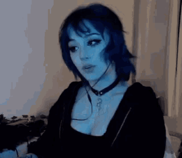 a woman with blue hair and a choker is sitting on a bed in a dark room .