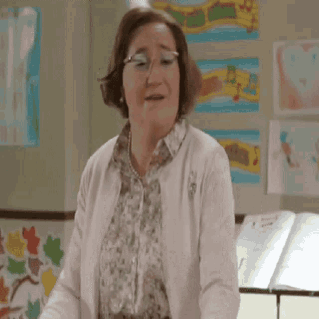 a woman wearing glasses and a pink cardigan is standing in front of a piano in a room .