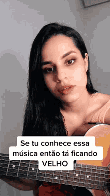a woman is holding a guitar with a caption that says se tu conhece essa musica então ta ficando velho