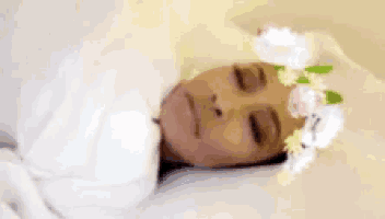 a woman is wrapped in a white blanket and wearing a flower crown on her head .