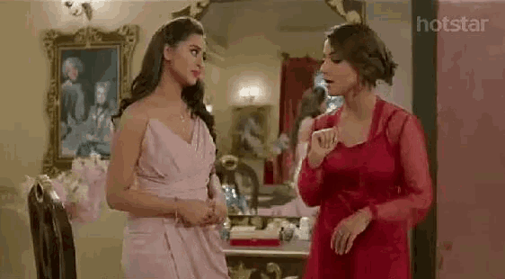 two women are standing next to each other in a room talking .