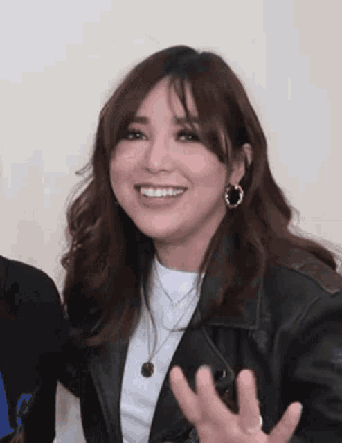 a woman wearing a leather jacket and earrings is smiling