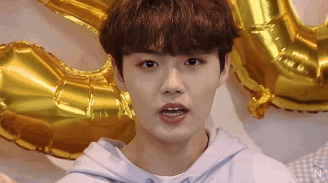 a close up of a person 's face with balloons in the background and the letter n in the corner