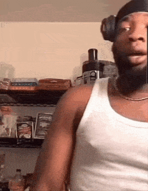a man wearing headphones and a white tank top is standing in front of a shelf in a kitchen .