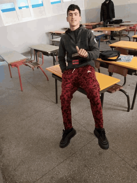 a young man sits on a bench in a classroom wearing a sweatshirt that says abercrombie & fitch