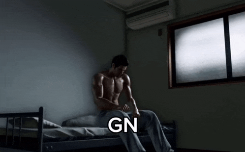 a shirtless man sits on a bed in a dark room with the word gn below him