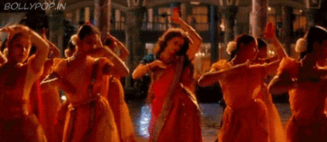 a woman in a red saree is dancing with other women in yellow dresses .