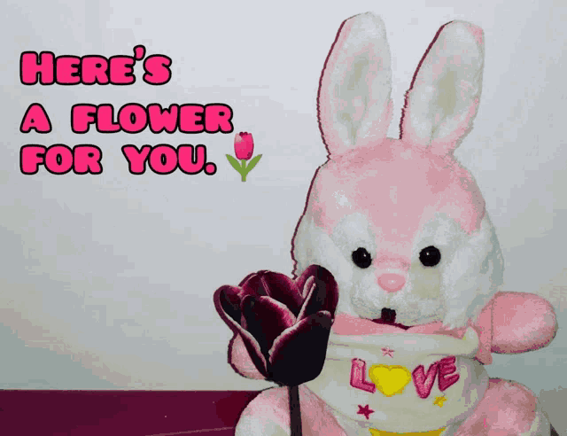 a pink and white stuffed bunny holding a flower with the words here 's a flower for you