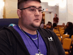 a man wearing glasses and a purple shirt is sitting in a row of chairs