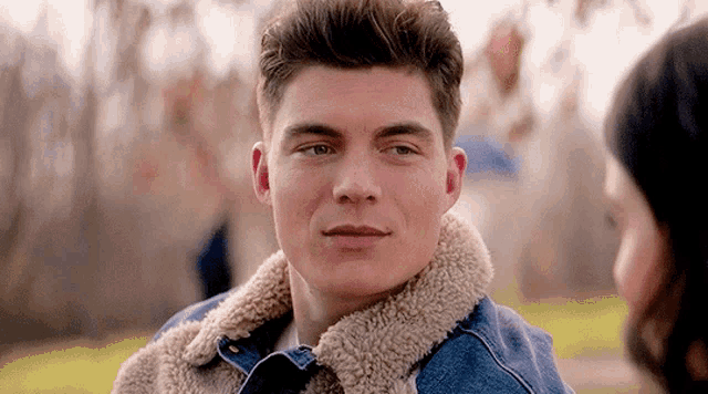 a young man wearing a denim jacket is looking at a woman .