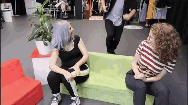 two women are sitting on a green couch and talking to each other .