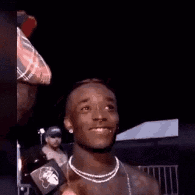 a young man wearing a pearl necklace and earrings is smiling while talking into a microphone .