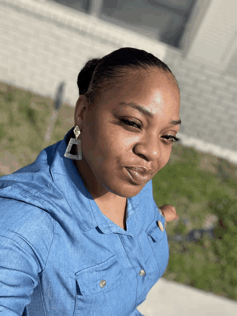 a woman wearing a denim shirt and earrings looks down