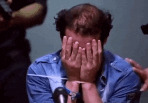 a man covering his face with his hands while wearing a blue shirt