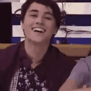 a young man in a maroon shirt and tie is laughing .