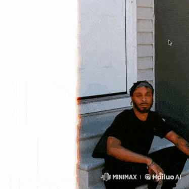 a man in a black shirt sits on the steps of a house in front of a window
