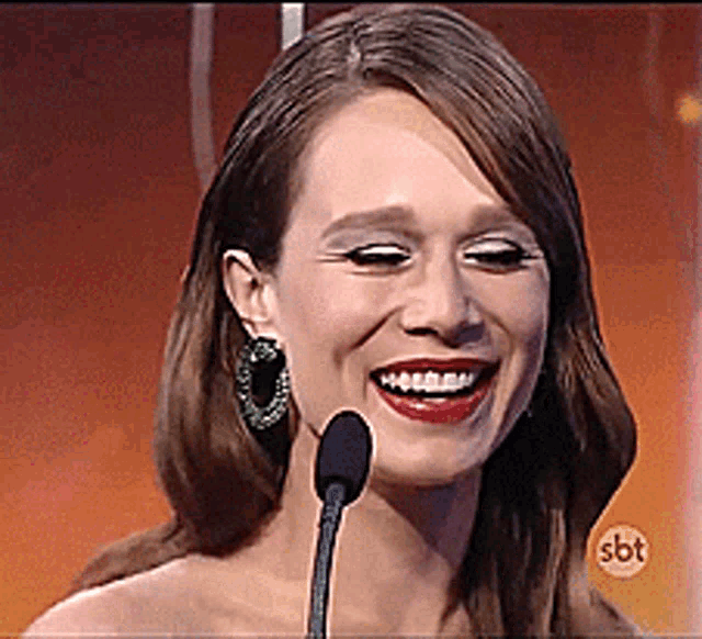 a woman is smiling in front of a microphone with sbt written on the bottom right