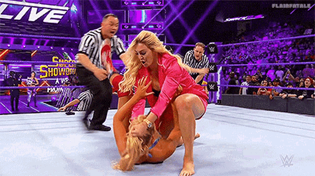 a woman is wrestling another woman in a wrestling ring while a referee watches .