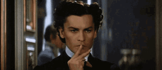 a man in a black suit is holding his finger to his lips .