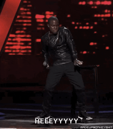 a man in a leather jacket is holding a microphone and saying heeeyy