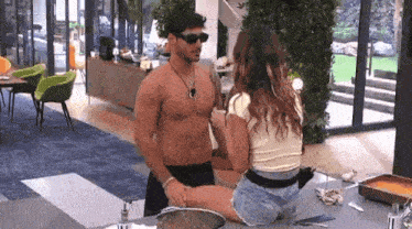 a man without a shirt is sitting on a woman 's lap on a kitchen counter .