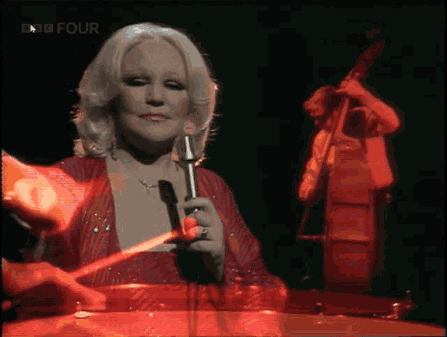 a woman in a red dress is singing into a microphone while a man plays a double bass in the background