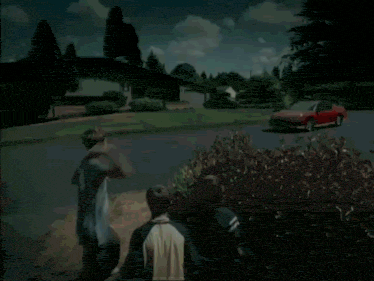 a red car is driving down a street with a group of people standing in front of it