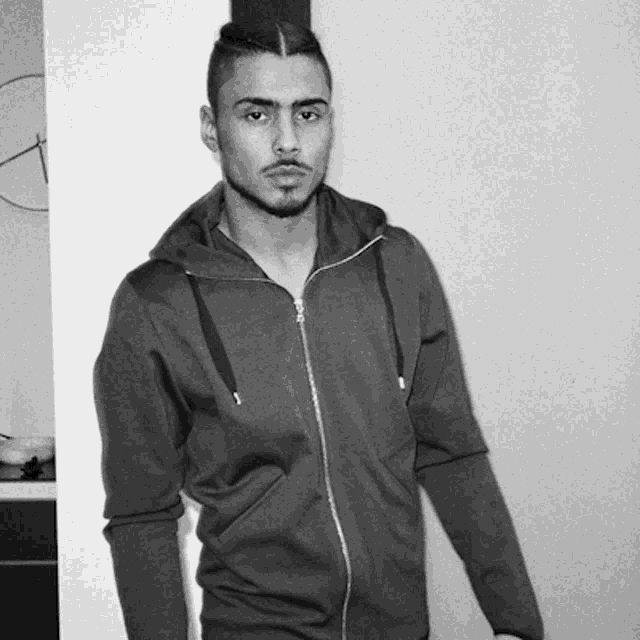 a man in a hoodie stands in front of a wall with a clock on it
