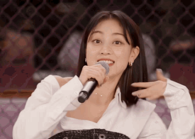 a woman is singing into a microphone while wearing a white shirt