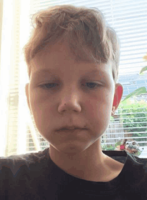 a young boy is making a sad face in front of a window .