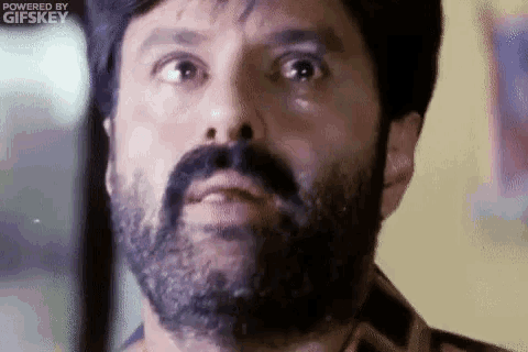 a man with a beard and mustache is looking at the camera with a tear coming out of his eye .