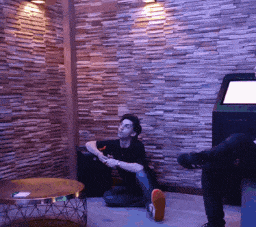 a man sits on the floor in a room with a brick wall