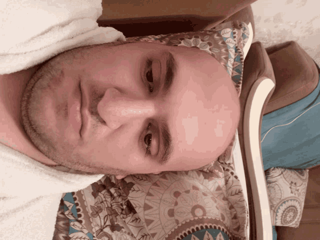 a bald man is laying on a couch with a floral blanket