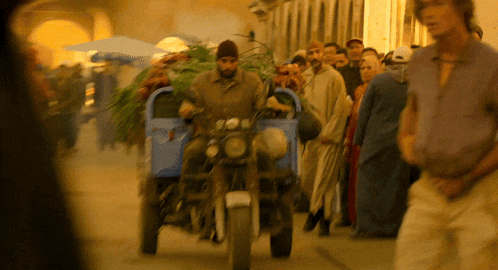 a man on a motorcycle pulling a cart full of trees