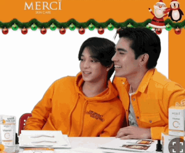 two men are sitting at a table with a sign that says merci skin care on it