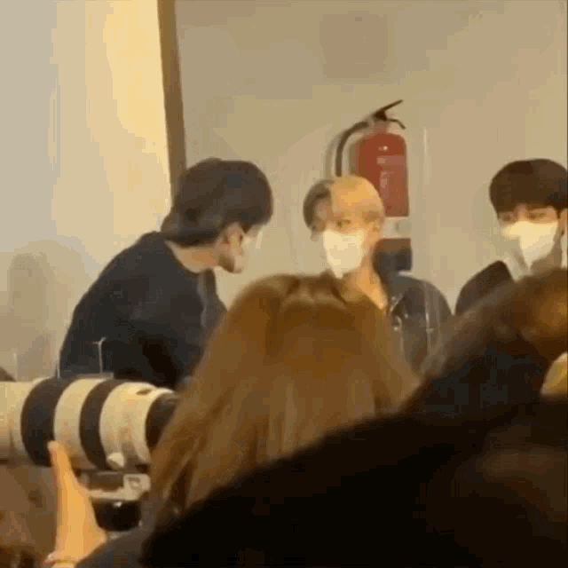 a group of people wearing face masks are standing in a room with a camera .